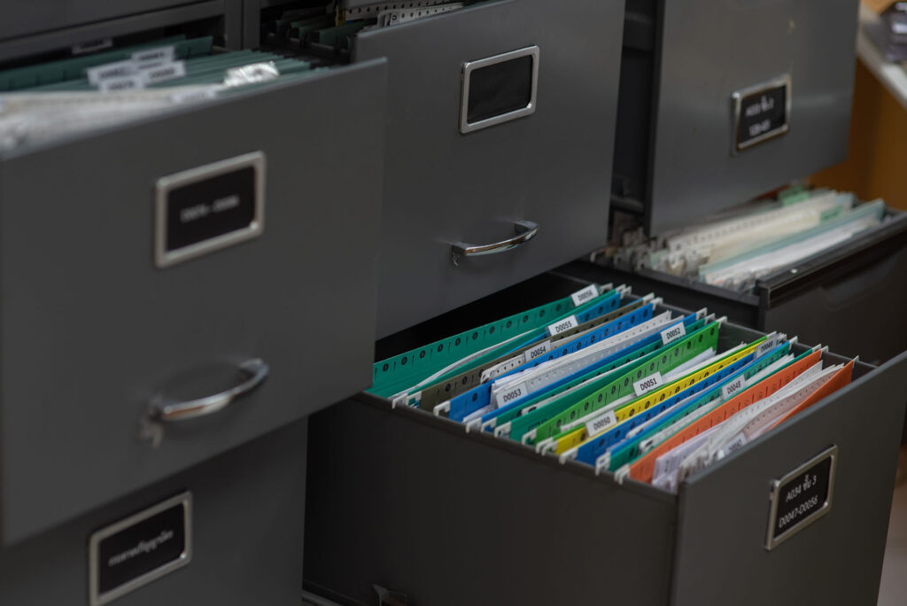 Experience neat, accessible organisation with grey filing cabinets featuring open drawers. Clearly labelled folders, sorted by colour and tab, make finding documents quick and easy. Drawer labels ensure effortless file retrieval.
