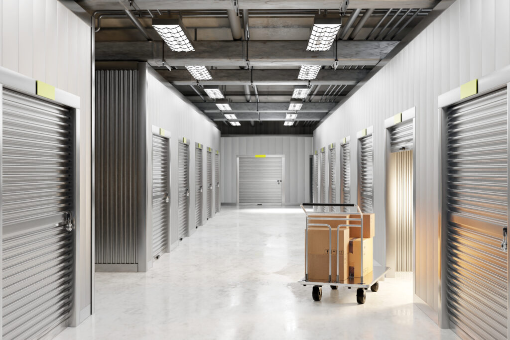 As you enter the storage facility, you'll notice a well-lit corridor lined with closed metal doors. For your convenience, a trolley with boxes is ready by an open unit to help you move and store your items easily.