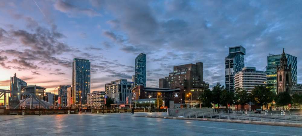 A sunset city skyline with modern and historic buildings under a partly cloudy sky; open paved area and railings in front, providing easy navigation for removals in Cheshire and ensuring a smooth urban moving experience.