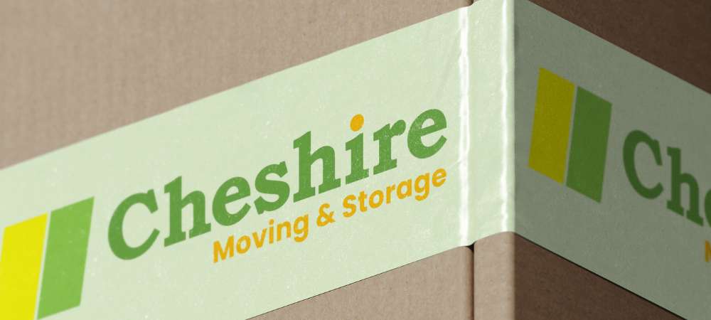 A close-up of a cardboard box sealed with green tape, clearly labelled "Cheshire Moving & Storage—your trusted partner for business removals in Cheshire" in green and orange text, with a yellow and green square logo.